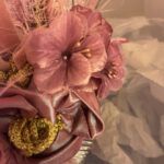 Close-up of a pink satin flower with a cluster of pink beads in the center and gold trim accents, as part of a decorative fabric piece.